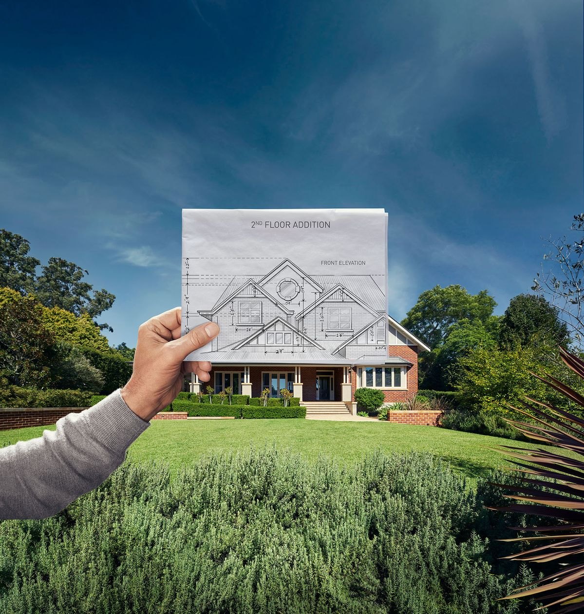 A hand holding an architectural elevation drawing in front of a house